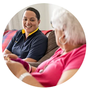 SW-smiling-and-elderly-knitting (1) Older woman at home knitting and chatting to a carer in uniform who is sitting on the couch.